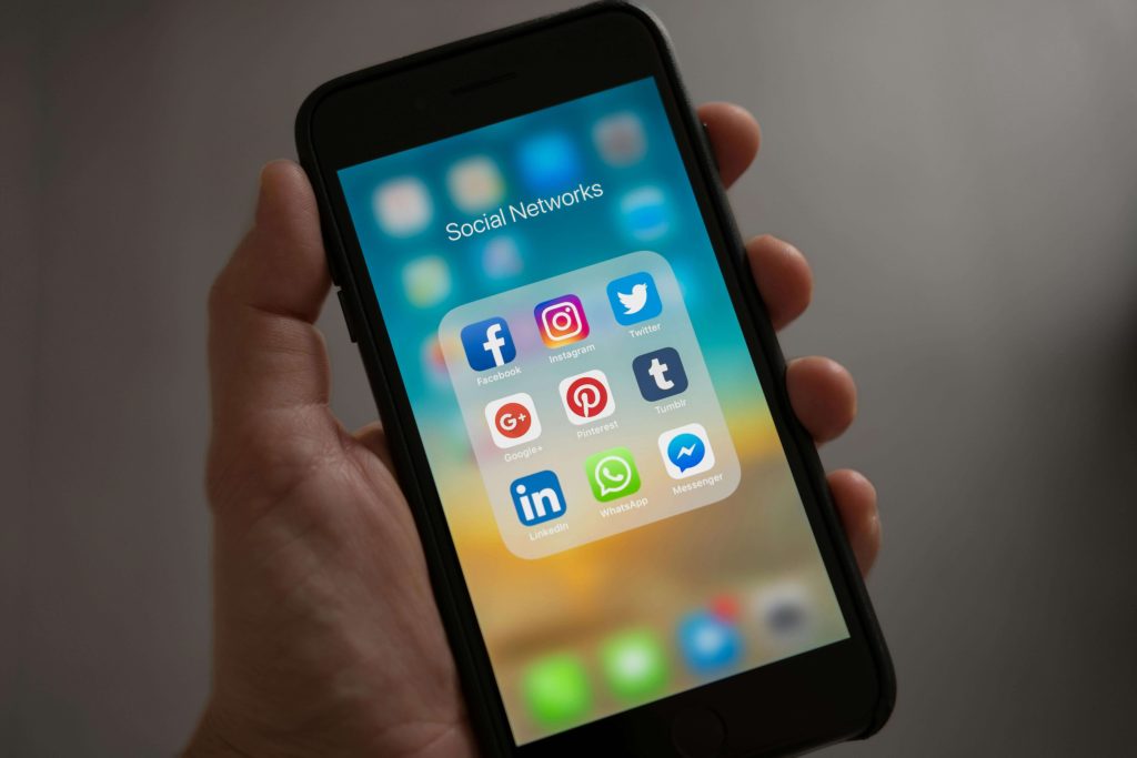 Ljudska ruka koja drži mobitel sa upaljenim zaslonom na kojem su ikone društvenih mreža - Facebook, Instagram, Twitter, Linkedin, WhatsApp, Messenger