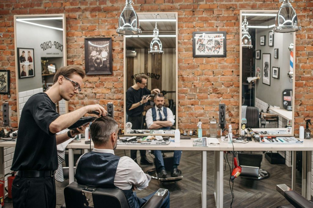 Frizerski salon za muškarce gdje vidimo muškog frizera koji šiša klijenta koji sjedi na stolici